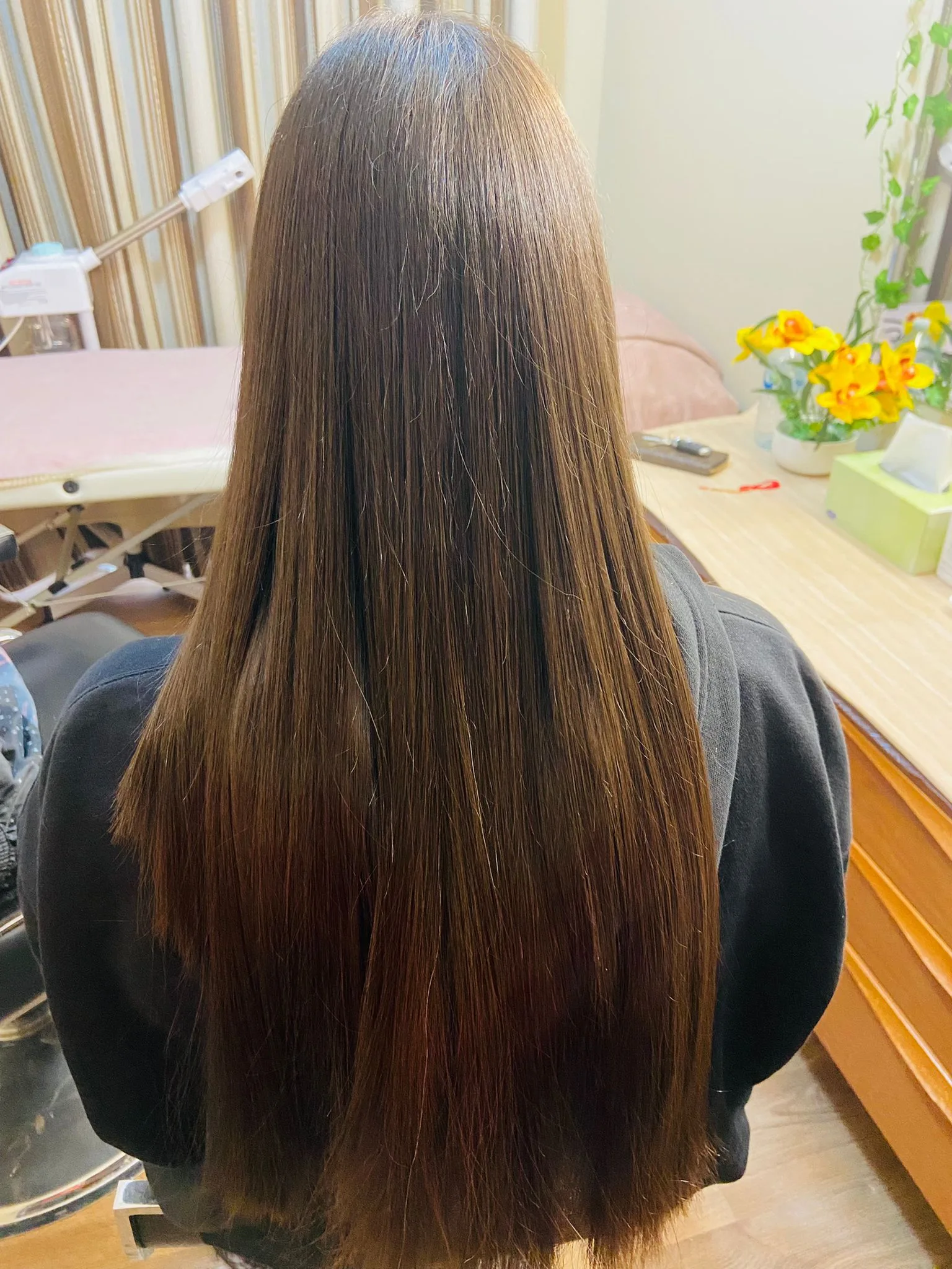 Inside the salon — mirror-straight blow-dry, striped curtains, yellow flowers and a tidy salon dresser in the background