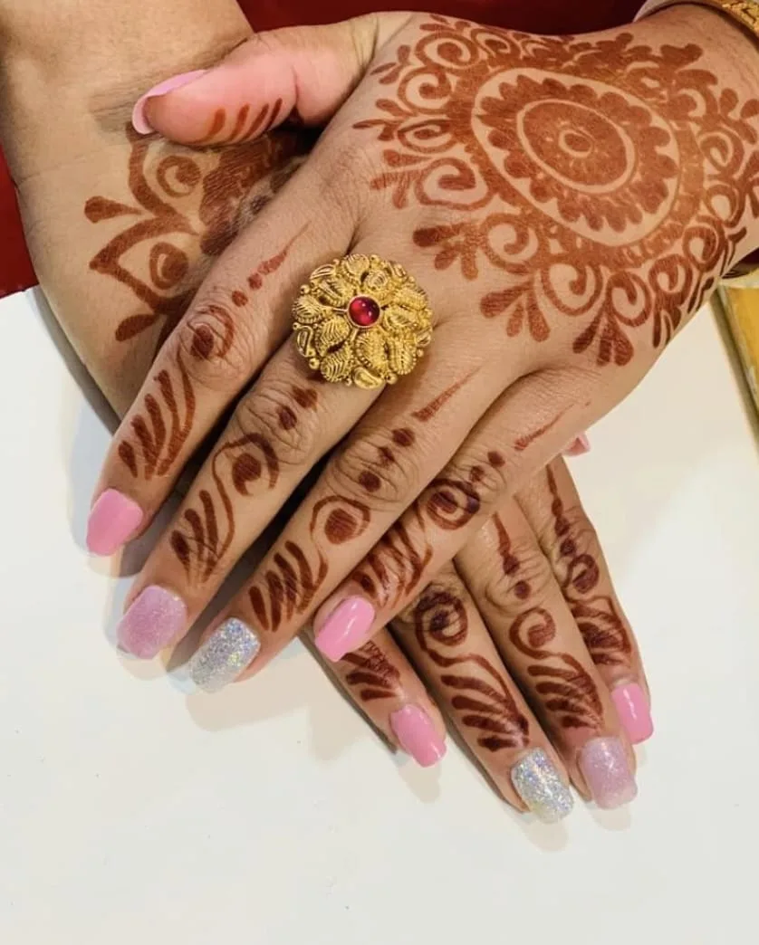 Intricate bridal mehndi across both hands with gold ring and glitter nails