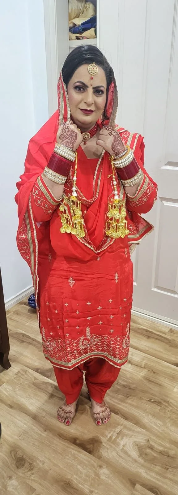 Full-length red bridal suit with kaleere, gold jewellery, mehndi and full makeup, standing on the salon floor